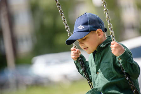 Russia, Saint Petersburg, 15.07.2020-boy in a cap riding on a swing in the cityのeditorial素材