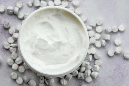 Close-up of a smooth moisturizer in a plastic jar on a blue background with white small stones on top. The concept of skin care.の写真素材
