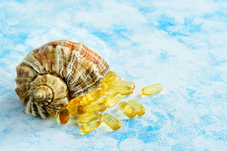 Golden fish oil capsules on a blue background - the concept of health and natural marine vitamins.の写真素材