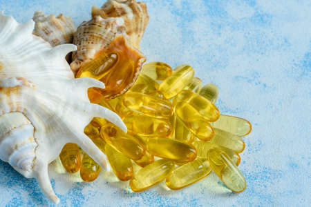 Golden fish oil capsules on a blue background - the concept of health and natural marine vitamins.の写真素材
