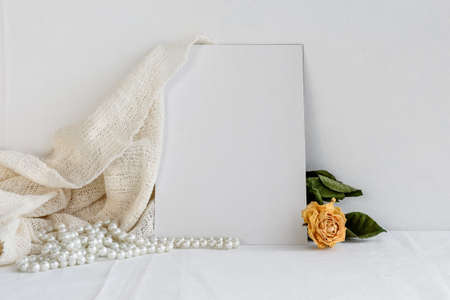 A blank white greeting card, a pearl necklace, and dried yellow roses on a white background. Romantic background for the invitation.の写真素材