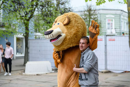 Russia, Gatchina, May 15, 2021: A man in a lion costume on a city street embraces and takes a photo with a guy. Advertising on the street. Work in advertising.のeditorial素材