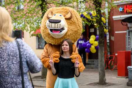 Russia, Gatchina, May 15, 2021: A man in a lion costume on a city street embraces and takes photos with passers-by. Advertising on the street. Work in advertising.のeditorial素材