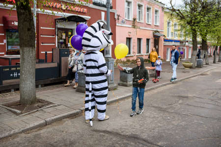 Russia, Gatchina, May 15, 2021: A man in a zebra costume on a city street greets passers-by and gives balloons to children. Advertising on the street.のeditorial素材
