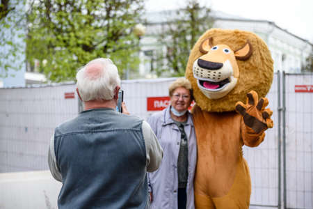 Russia, Gatchina, May 15, 2021: A man in a lion costume on a city street embraces and takes photos...