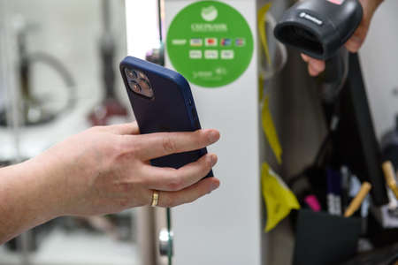Russia, May 15, 2021: The seller serves customers in the store. Trade in compliance with sanitary standards. The salesman in the mask is a cash register. Reading the payment from your smartphone via the app.のeditorial素材