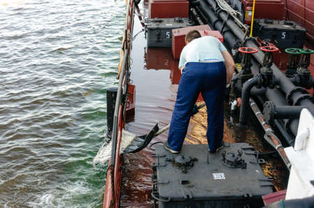 Russia, St. Petersburg, May 2021: A working seaman of an oil tanker removes water from the deck in the bay in the portのeditorial素材