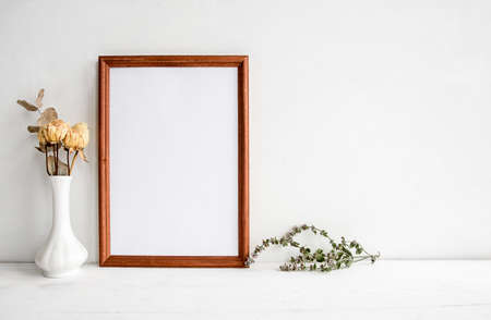 A wooden empty photo frame on a white table and flowers in a vase. A fashionable wedding or holiday banner.の写真素材