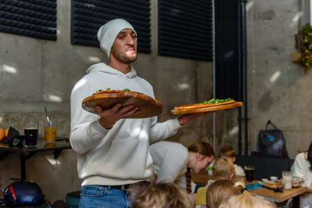 Russia, Gatchina, November 20212: A young guy waiter delivers pizza to the tablesのeditorial素材
