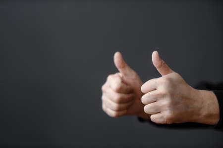 Two male hands give a thumbs up on a dark background. Close up and copy spaceの写真素材