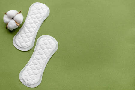 Cotton flower on a green paper background and sanitary pads for women, top view. The concept of hygiene and women's healthの写真素材