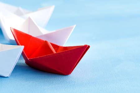 The concept of leadership. The red flagship paper ship leads the others ahead on a blue background.の写真素材