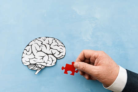 hand is trying to connect the missing puzzle of the human brain on a blue background. mental health...