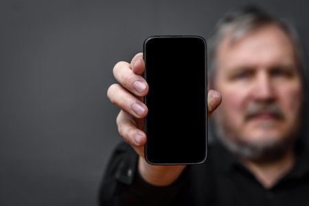 man holds a smartphone with an empty black screen on a dark backgroundの写真素材
