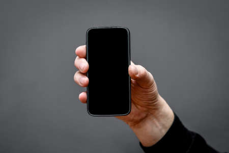 smartphone frame with an empty black screen on a dark background in a man's hand.
