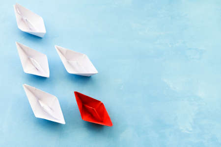 The concept of leadership. The red flagship paper ship leads the others ahead on a blue background.の写真素材