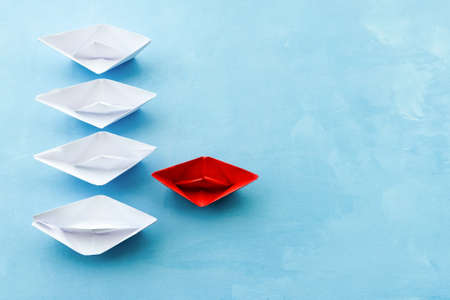 The concept of leadership. The red flagship paper ship leads the others ahead on a blue background.
