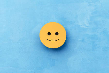 Yellow slightly smiling face on a blue background. The concept of mood selection and customer feedback. Copy space, business and emotionsの写真素材