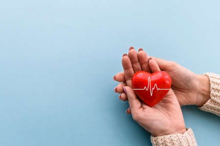red heart in women's hands on a blue background. The concept of health, donation, volunteering and health insurance.の写真素材