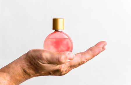 A bottle of women's perfume in a man's hand on a white backgroundの写真素材