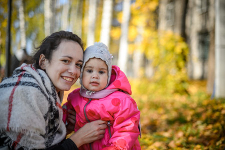 young mom with little daughter in the park in autumn close-upの写真素材