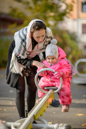 a young mother with a little daughter on a swing in the yard in autumnの写真素材