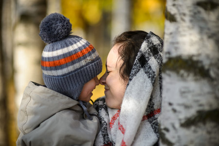 Happy young mother with a young son in her arms in an autumn park - close-upの写真素材