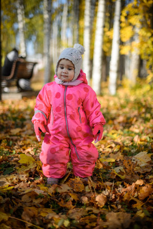 A one-year-old girl in a red jumpsuit on a walk in autumnの写真素材
