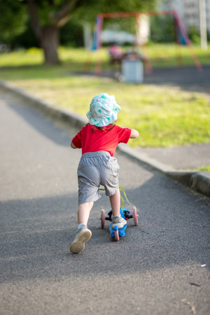Little girl on a scooter alone in a park in summerの写真素材
