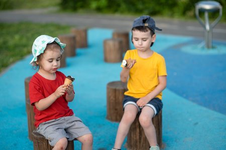Two little children, boy and girl, eating ice cream in the parkの写真素材