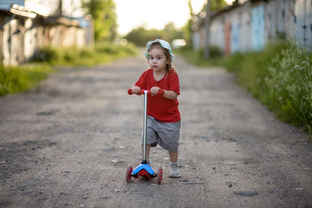 Cute little girl riding a scooter in the park at sunsetの写真素材