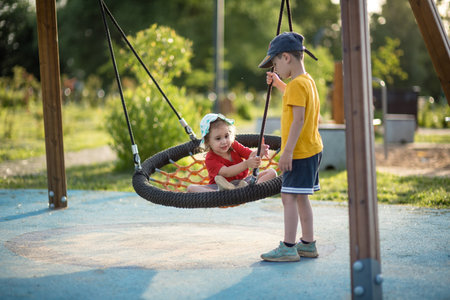 Two little children, boy and girl, playing on a swing in the parkの写真素材