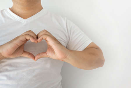 The man in the white shirt put his fingers together in a heart shape on his chest. Show love and charm With a white backgroundの写真素材