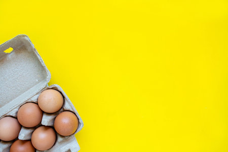 Closeup brown egg in a cardboard box from a supermarket on a yellow background.の写真素材