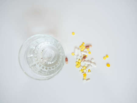 Multi colored pills with a glass of water placed on a white backgroundの写真素材