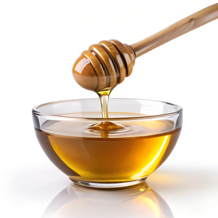 Honey dripping from a wooden honey dipper into a bowl isolated on white backgroundの素材