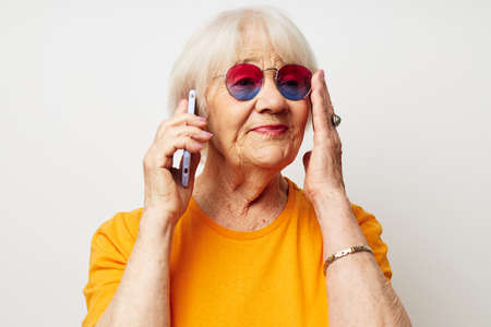 elderly woman in casual t-shirt sunglasses talking on the phone isolated backgroundの写真素材