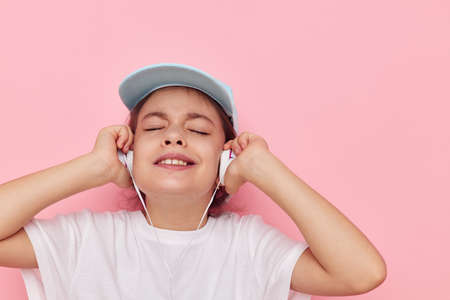 Portrait of happy smiling child girl headphones in a white t-shirt and a cap pink backgroundの写真素材