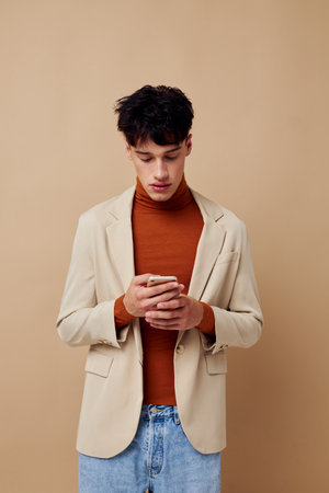 portrait of a young man in a beige jacket talking on the phone light background unalteredの写真素材