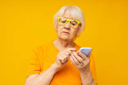elderly woman in casual t-shirt communication by phone yellow background