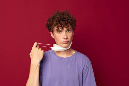 A young man in purple t-shirts medical mask in hands safety isolated background unaltered