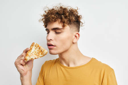 handsome guy in a yellow t-shirt eating pizza isolated background