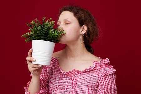 Young woman in green shorts flowerpot posing red background unalteredの写真素材