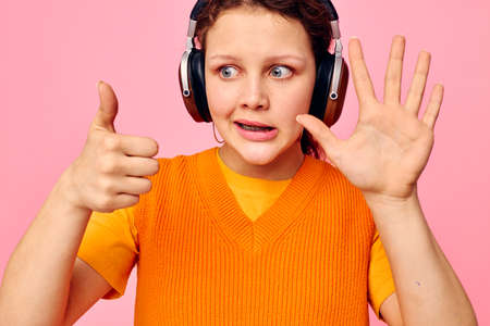 pretty woman listening to music with headphones orange sweater emotions fun cropped view unaltered