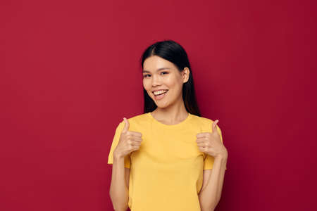 woman with Asian appearance gestures with his hands in a yellow t-shirt casual wear red background...
