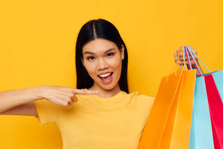 pretty brunette in a yellow T-shirt with multicolored shopping bags yellow background unalteredの写真素材