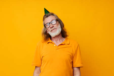 Portrait of happy senior man in a yellow t-shirt with a cap on his head fun yellow backgroundの写真素材