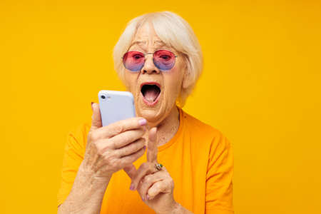 elderly woman in fashionable glasses with a smartphone close-up emotionsの写真素材