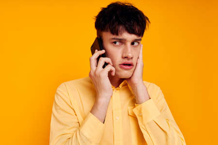 handsome man in a yellow shirt talking on the phone close-upの写真素材