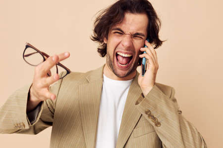 Cheerful man in a suit posing emotions talking on the phone beige backgroundの写真素材